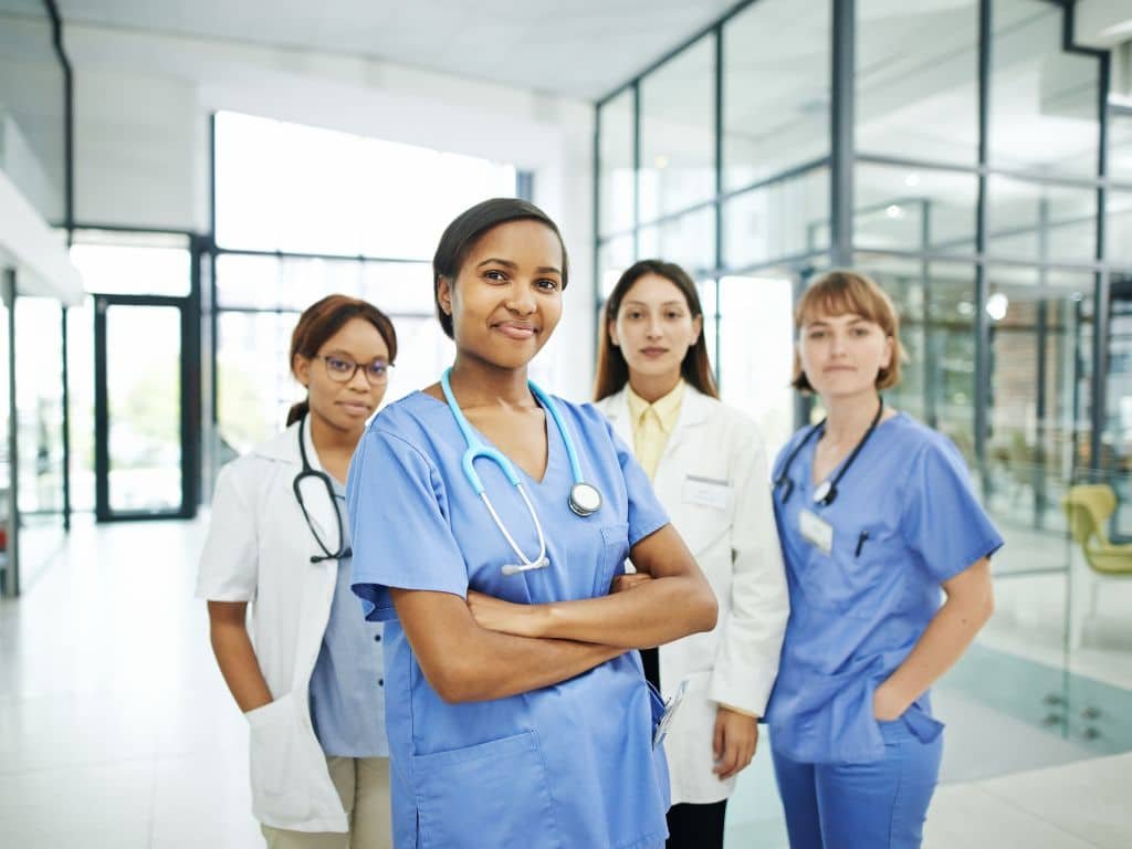 Four healthcare professionals, three in scrubs and one in a white coat, stand together in a modern medical facility—your trusted team to find a Las Vegas doctor or explore Direct Primary Care options.