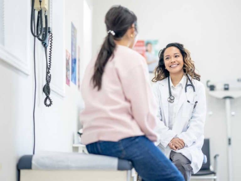 A doctor wearing a white coat and stethoscope smiles while talking to a patient during their first appointment in a functional medicine Las Vegas office.