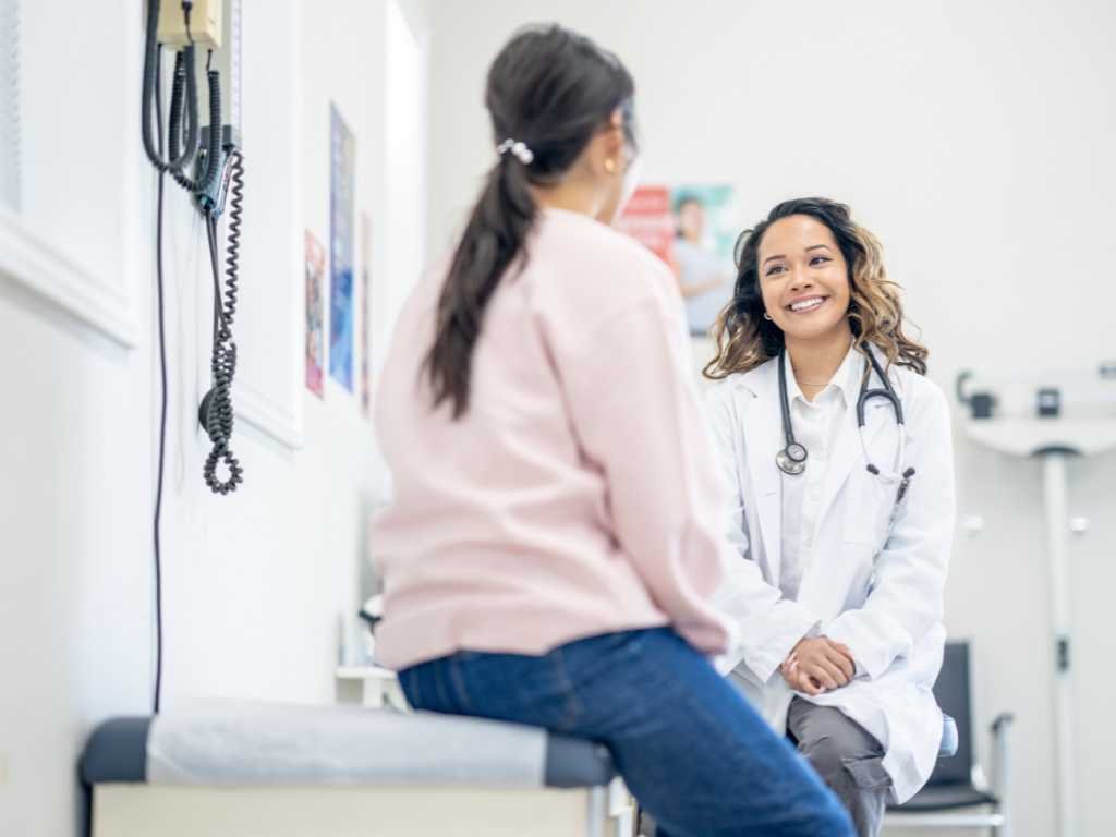 A doctor wearing a white coat and stethoscope smiles while talking to a patient during their first appointment in a functional medicine Las Vegas office.