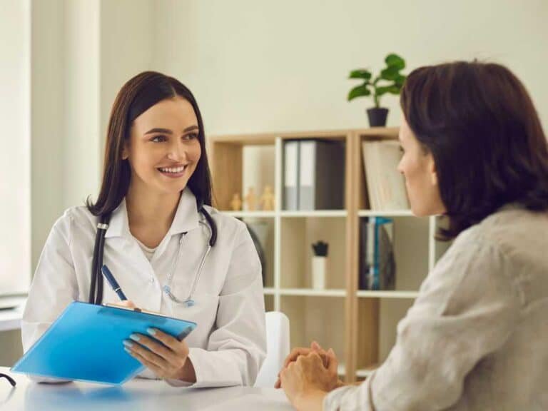 A doctor with a stethoscope smiles while holding a clipboard and discussing functional medicine cost with a patient in a Las Vegas office setting.