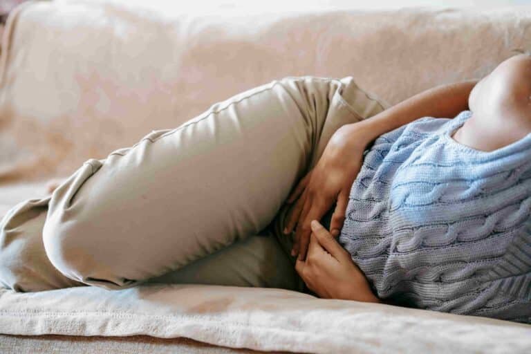 Person lying on a couch, curled up on their side with hands holding their stomach, suggesting discomfort or pain—potentially seeking Functional Medicine for Gastro Disease relief.
