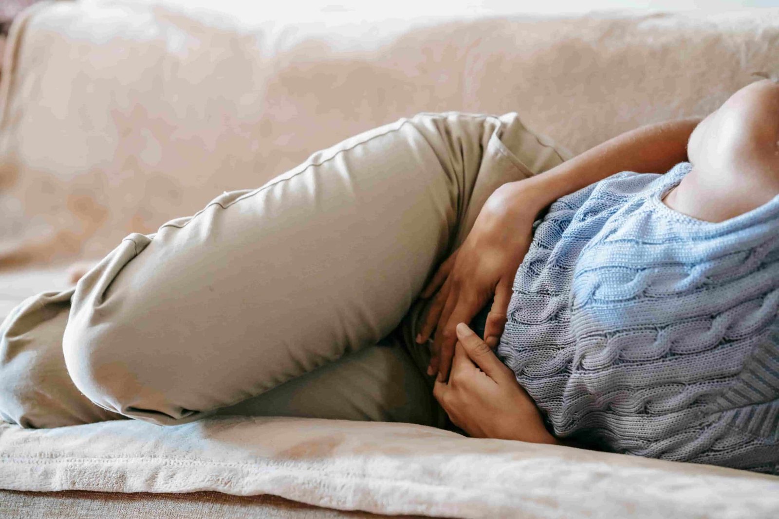 Person lying on a couch, curled up on their side with hands holding their stomach, suggesting discomfort or pain—potentially seeking Functional Medicine for Gastro Disease relief.