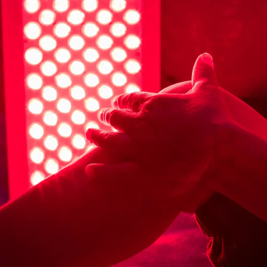 A person massages a leg in front of the MitoPRO X | Red Light Therapy Panel Series, which emits bright red LED light therapy.