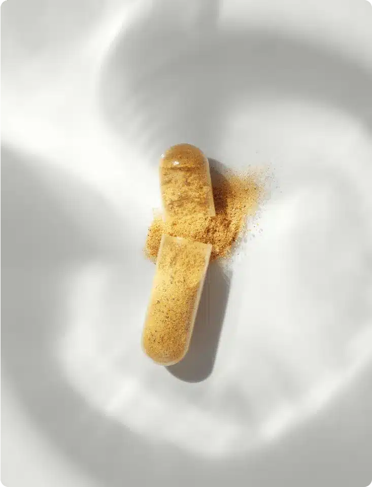 A transparent capsule from the Fullest Hair Kit, containing yellow powder and partially opened with some powder spilling out, lies on a softly textured white surface.