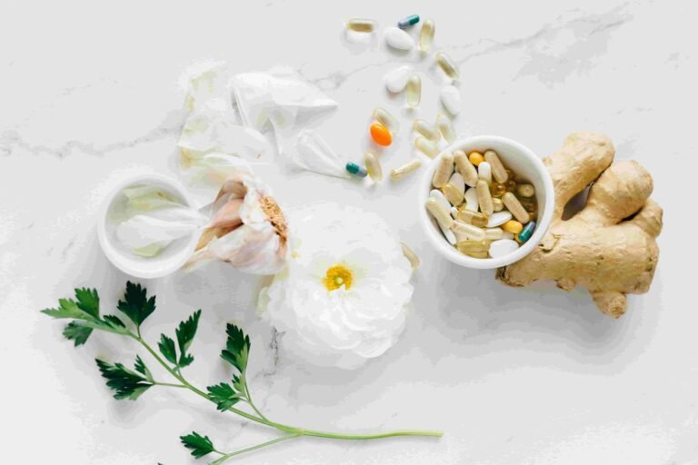 Assorted pills, a bowl of supplements, ginger root, a white flower, garlic, and parsley sprig arranged on a white surface—elements often considered in discussions about the cost of Functional Medicine in Las Vegas.