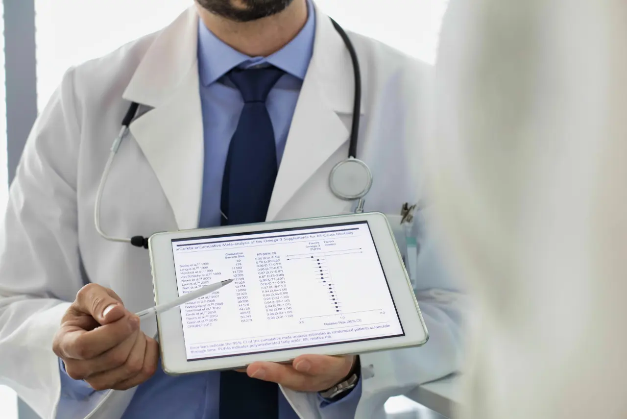 A doctor in a white coat and stethoscope holds a tablet displaying medical data, pointing at the screen while discussing Functional Medicine Las Vegas options with a patient.